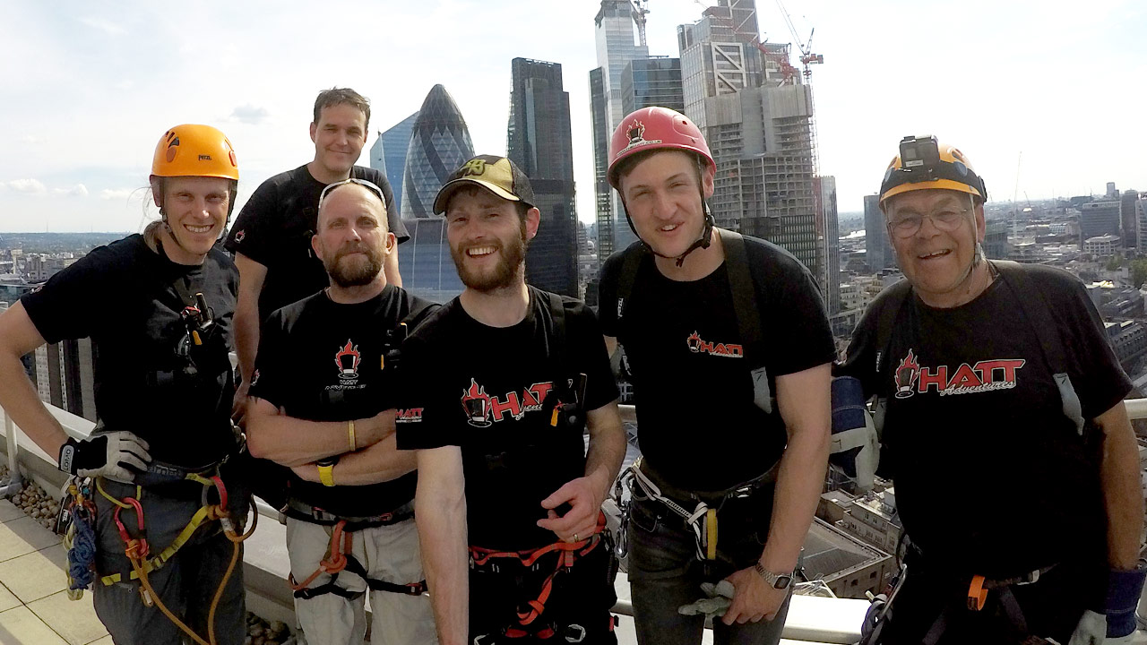 image shows a team of Hatt adventures instuctors at the top of a building in central London, they are wearing safety equipment like helmets and harnesses